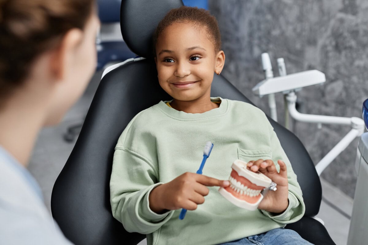black little girl in dental chair holding tooth