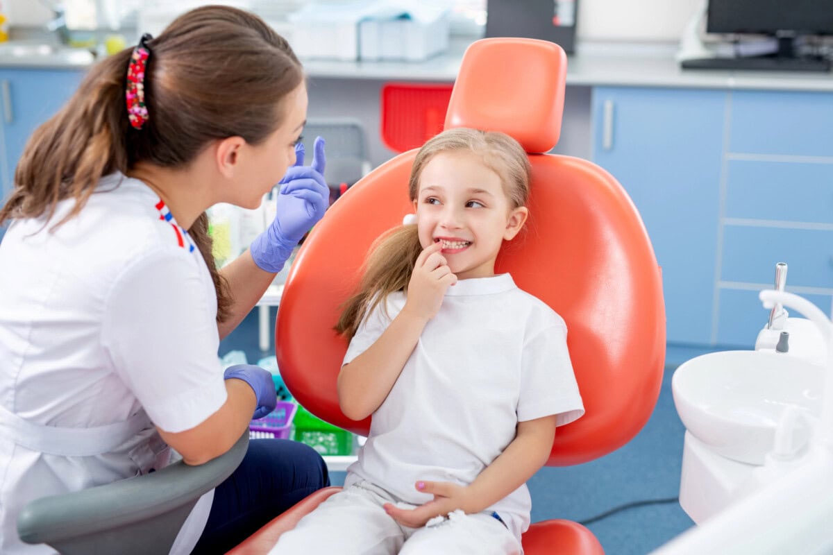 Pediatric dentist talks to a little girl and tells her how to take care of her teeth. beautiful girl is smiling in the dentist's office.