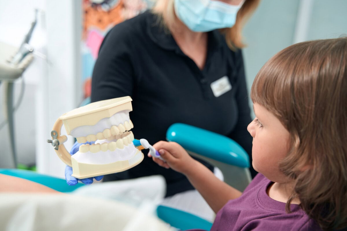 female child learning to clean teeth in dental cli